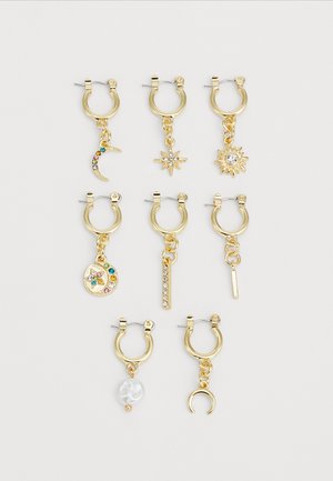 Boucles d'oreilles en or avec différents charms : lune, étoile, soleil, accents de pierres précieuses, et une avec une perle ; finitions texturées et brillantes.