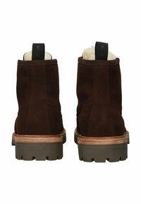 Rudono suede kulkšnies batai su šeršiamo pamušalu, juodu kilpeliu ir tvirtu guminio pado, turinčio gilius protektorius, kad būtų užtikrintas sukibimas.