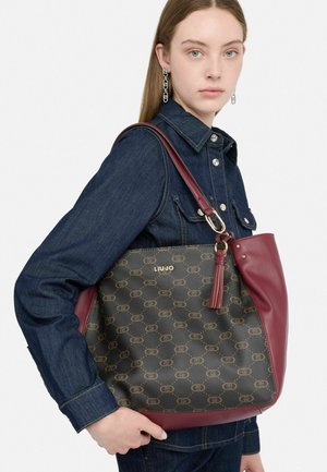 Sac à main en cuir marron et bordeaux avec un motif monogramme, un logo doré et un accent à pampilles. Il présente une forme structurée et des poignées robustes.