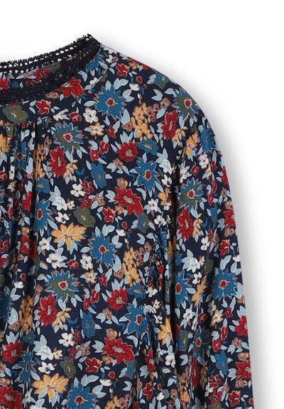 Haut en tissu à motif floral présentant une base bleu marine foncé, avec des fleurs rouges, bleues, jaunes et vertes vives, et un col en dentelle noire texturée.