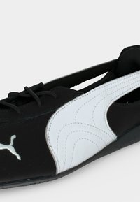Μαύρο-άσπρο Puma slip-on sneaker με κορδόνια και χαρακτηριστική κυρτή ρίγα στο πλάι, εμφανιζόμενο από κοντινή γωνία.