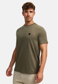 Olivegrünes Kurzarm-T-Shirt aus weichem Stoff, mit rundem Ausschnitt und einem kleinen schwarzen Logodetail auf der Brust.