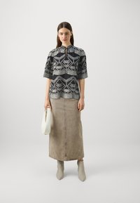 Camicia a righe in bianco e nero con scollatura a chiave, abbinata a una gonna midi in denim beige e stivaletti grigi chiari con punta. Tiene una borsa bianca.