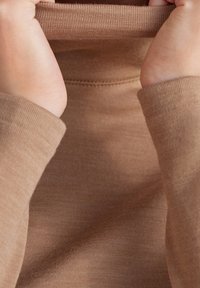 Pull à col roulé marron avec une texture lisse et des poignets côtelés, présentant une vue en gros plan du col roulé et des détails de couture du tissu.