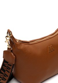Borsa in pelle marrone con una finitura testurizzata, dotata di una cerniera dorata e di una tracolla rimovibile con un motivo. Dettaglio del logo in rilievo ben visibile.