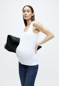 Λευκό αμάνικο τοπ με στρογγυλεμένο ντεκολτέ, εφαρμοστή γραμμή, φορεμένο με σκούρο τζιν. Το πρόσωπο κρατά μια μαύρη τσάντα με κλείσιμο με φερμουάρ.