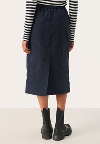 Navy midi-rok met een gekreukt textuur, een elastische tailleband en een split aan de achterkant. Gepaard met zwarte chunky enkellaarsjes.