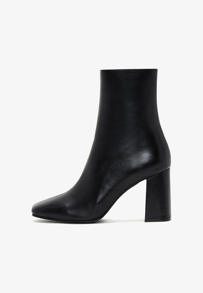 Bottine en cuir noir avec un bout pointu et une texture lisse. Elle possède un talon carré épais pour plus de stabilité.