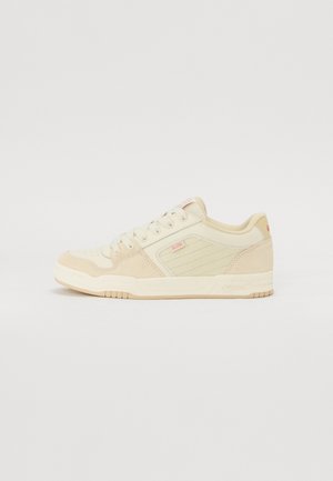 Beige sneakers with a mix of smooth leather and suede, featuring a textured side panel, round toe, and a padded collar, showing muted accents.