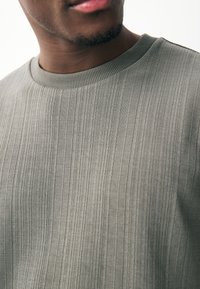 Grijze katoenen crewneck trui met verticale, geprofileerde strepen, geribde halslijn en gladde stof. Close-up van het materiaal.