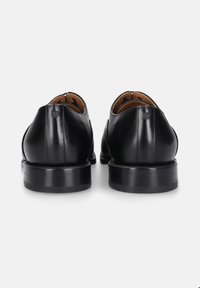 Ein Paar polierte schwarze Lederhalbschuhe, von hinten betrachtet, zeigt genähte Fersen und gestapelte schwarze Sohlen auf weißem Hintergrund.