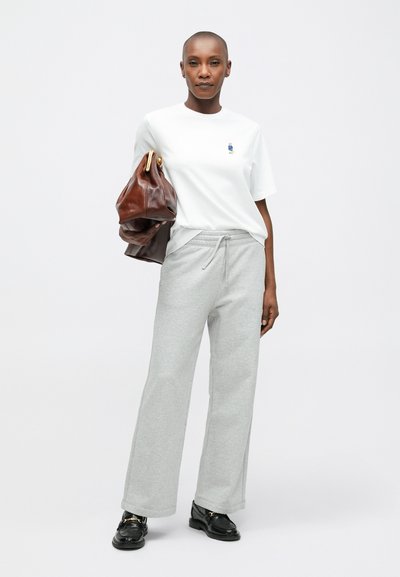 Λευκό μπλουζάκι με μικρή μπλε γραφιστική, γκρι φόρμες με κορδόνι και καφέ δερμάτινη τσάντα. Μαύρα loafers με χρυσές λεπτομέρειες.