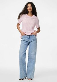 Světle růžový pletený svetr s krátkými rukávy, zdobený texturovaným vzorem. V kombinaci s modrými džíny s vysokým pasem a volným střihem a černými sandály.