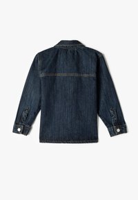 Chaqueta de mezclilla oscura, vista trasera. Presenta mangas largas, puños abotonados y costuras en contraste. Cuello clásico con una textura suave.