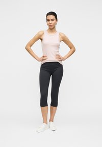 Débardeur rose pâle et leggings capri noirs. Le tissu semble lisse. Le débardeur a un col arrondi, tandis que les leggings sont ajustés.