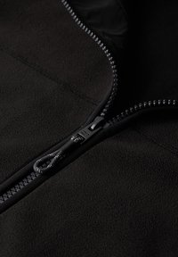 Tessuto in pile nero con una texture liscia, dotato di una cerniera resistente lungo il bordo e di un gancio per tirare. Dettagli delle cuciture visibili.