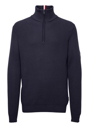 Tmavomodrý rebrovaný sveter s vysokým golierom, zipsovým zapínaním a malým logom na rukáve. Obsahuje kontrastné červené a biele detaily vo vnútri goliera.