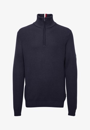 Tmavomodrý rebrovaný sveter s vysokým golierom, zipsovým zapínaním a malým logom na rukáve. Obsahuje kontrastné červené a biele detaily vo vnútri goliera.