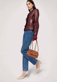 Vínově červené kožené sako s přiléhavým střihem, modré džínové kalhoty, krémové lodičky s špičatou špičkou a malá hnědá kabelka.