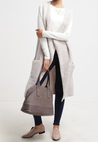 Ljusgrå, fluffig lång väst med två framfickor, matchad med mörkblå skinny jeans. Bär en strukturerad grå handväska och har på sig beige ballerinas.