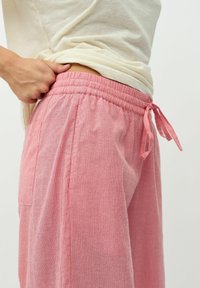 Lätta, rosa randiga byxor med elastisk midja och snörning. Har sidfickor och en avslappnad passform. Mjuk tygkänsla.