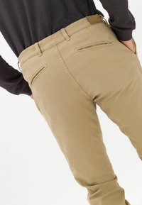 Beżowe spodnie o dopasowanym kroju, wykonane z miękkiej bawełny. Posiadają dwie tylne kieszenie oraz brązową skórzaną łatę na pasku.
