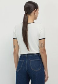 Top bianco a maniche corte con bordo nero, abbinato a jeans a vita alta blu scuro con tasche posteriori e una classica texture in denim.