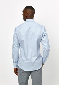 Lichtblauw overhemd met een klassieke kraag, lange mouwen en knopenmanchetten. Een gladde stof met een getailleerde pasvorm en een afgeronde zoom.