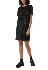 Czarna sukienka z cekinami, z krótkimi rękawami, okrągłym dekoltem i luźnym krojem. Połączona z masywnymi czarnymi butami i skarpetkami, tworząc warstwowy look.