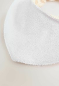 Bavoir pour bébé en tissu éponge blanc doux, fixé par une bande élastique pâle à fronces, posé sur une surface neutre.