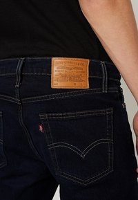 Mörkblå denimjeans med en läderlapp märkta "Levi Strauss & Co." och gula sömmar som detaljer på bakfickorna.