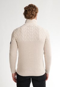 Maglione beige lavorato a maglia con collo alto, caratterizzato da texture a motivo foglia sui spallacci e orlo e polsini a costine.