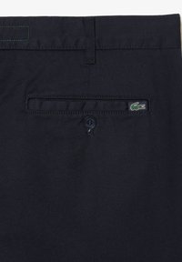 Pantalones de mezcla de algodón azul marino con un bolsillo trasero con botón y un logo bordado en verde. Textura suave con detalles sutiles de costura.