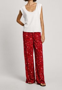 Top bianco a maniche corte abbinato a pantaloni larghi rossi con motivo floreale, caratterizzati da una texture liscia e gambe ampie.
