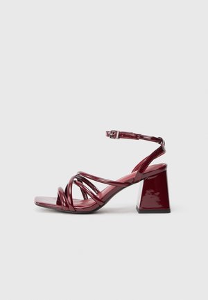 Sandalias de tacón burdeos de charol con punta cuadrada, que cuentan con múltiples tiras entrelazadas y un tacón grueso. Correa en el tobillo ajustable.