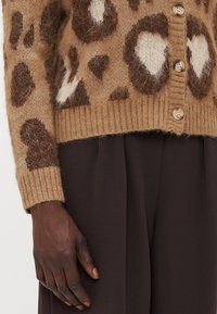 Leopardmønstret cardigan i tan og brun, med en fuzzy tekstur, ribbede manchetter og træknapper langs fronten.