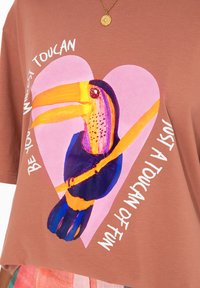 Hnědé bavlněné tričko s barevným grafikou tukan v růžovém srdci a s textem "Buďte svým nejdivočejším tukánem, jen trošku zábavy."