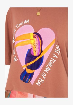 Brązowa koszulka bawełniana z kolorową grafiką tukan w kształcie różowego serca z napisem "Bądź swoim dzikim tukanem, po prostu tukanem zabawy."