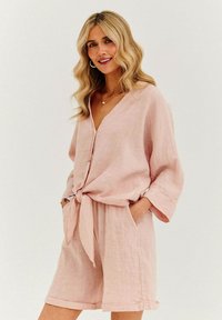 Svetloružový ľanový outfit s voľným topom s výstrihom do V a viazaním vpredu, doplnený o zodpovedajúce šortky s ohrnutými lemami.