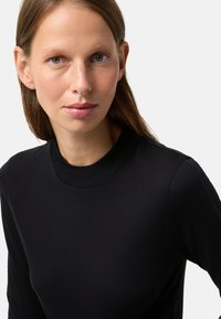 Schwarzes Langarmshirt mit hohem Kragen aus weichem Stoff. Es hat eine taillierte Passform und eine glatte Textur.