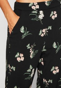 Pantalons en tissu noir ornés d'un motif floral avec des accents rose et vert. Comprend des poches latérales et une texture lisse.