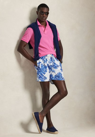 Ροζ πόλο πουκάμισο, λευκό και μπλε σορτς με λουλουδάτο σχέδιο, μπλε σκούρα πουλόβερ καλοκαιρινό φορεμένο στους ώμους και μπλε σκούρα εσπαντρίγιες.