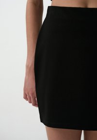 Jupe mini noire en tissu lisse, avec une silhouette ajustée et un ourlet net. Légèrement extensible pour un confort optimal et une grande liberté de mouvement.