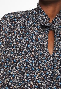 Patterned blouse featuring a dark navy background with small white, blue, and brown floral prints. Keyhole cutout at the neck. Lightweight fabric.