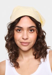 Puha anyagból készült sárga-fehér csíkos sapka, laza fazonú, enyhén leengedett formával és texturált felülettel.