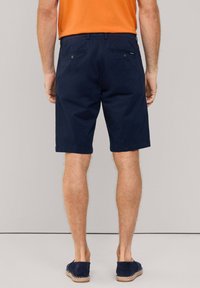 Pantaloni corti blu navy realizzati in tessuto leggero, con vita piatta, tasche laterali e posteriori, e orlo appena sopra il ginocchio.