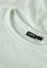 Lichtgroen kortemouwen shirt met ribbeltextuur, voorzien van een ronde halslijn en een klein ruitpatroon. Etiket toont merk LMTD, maat XS.