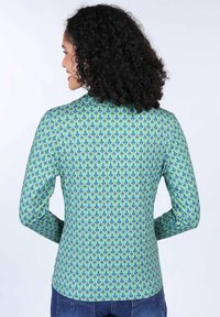 Langärmliges Hemd in Teal und Grün, mit einem geometrischen Muster und blauen sowie roten Akzenten. Glatte Textur, taillierte Passform und Rundhalsausschnitt.