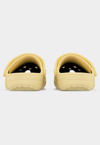 Φωτεινά κίτρινα παπούτσια τύπου clogs με τρύπες αερισμού και υφασμένα πέλματα, εμφανιζόμενα από πίσω σε λευκό φόντο.