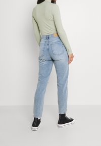 Top de manga larga acanalado en verde claro combinado con jeans de tiro alto en azul claro y zapatillas altas negras, con bolsillos traseros y un corte clásico.